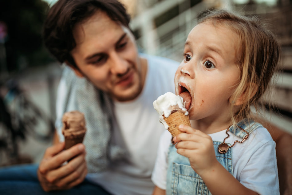 Father and daughter licking ice cream in public park