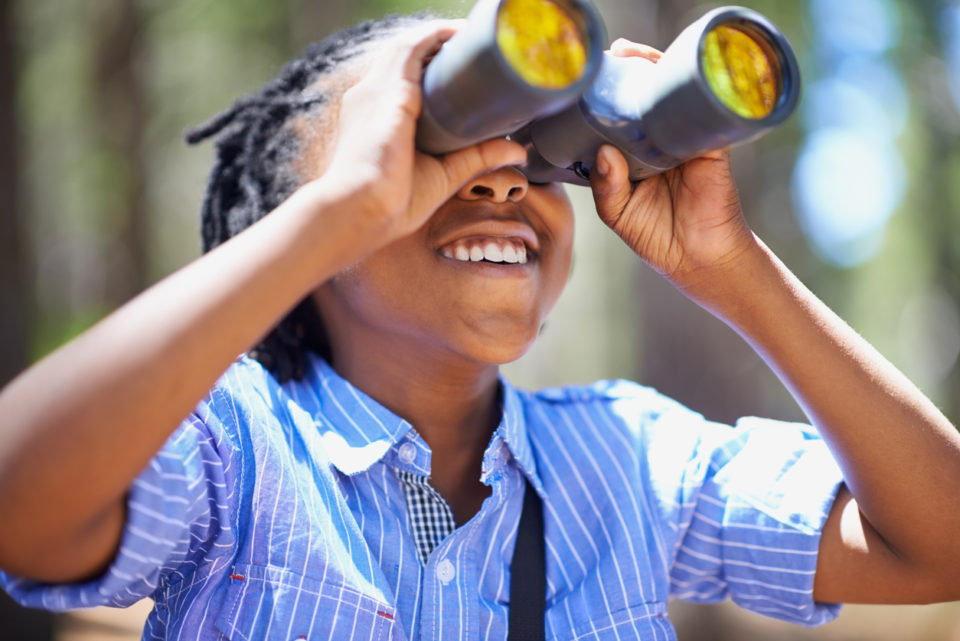 Shot of a young boy out in the woods with a pair of binoculars