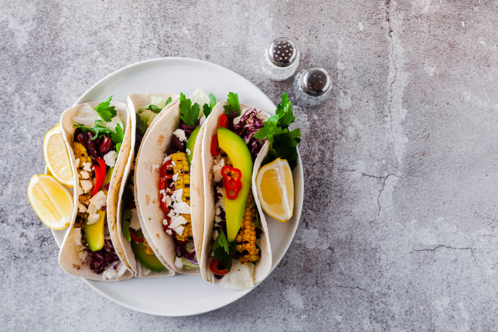 Mexican tacos with avocado, grilled corn, red cabbage slaw and chili salsa on wooden board black shale table. Recipe for Cinco de Mayo party. Top view. Copy space background