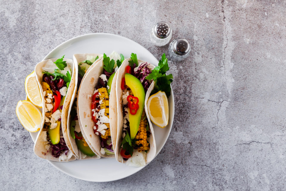 Mexican tacos with avocado, grilled corn, red cabbage slaw and chili salsa on wooden board black shale table. Recipe for Cinco de Mayo party. Top view. Copy space background